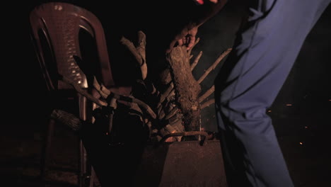 a bonfire burns brightly at night, with logs and chairs around in a slow-motion scene