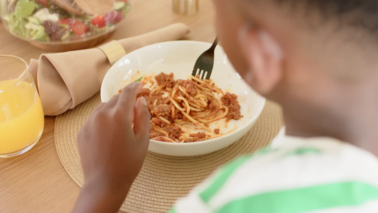 Affamato, un bambino sta prendendo una forchetta nera, arrotolando la pasta e portando la forchettata alla bocca per mangiare.