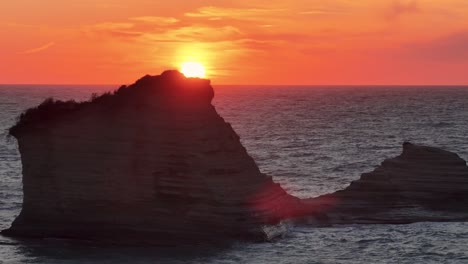 captivating mediterranean sunset: the sun dips below the horizon, painting the sky in fiery orange hues, casting dramatic silhouettes of coastal rock formations against the glistening sea.
