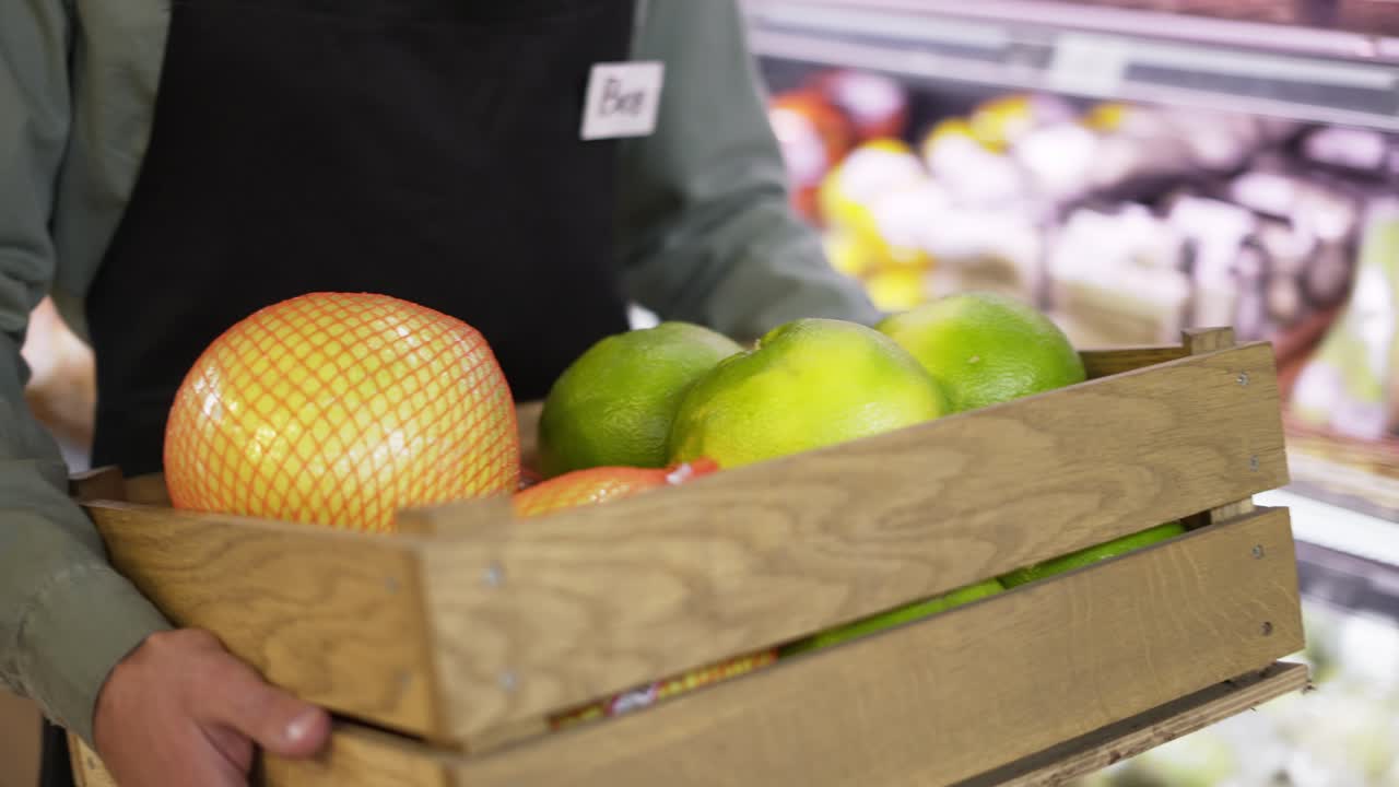 아프론 을 입은 남성 의 클로즈업. 손 은 실내 카운터 를 따라 채소 의 나무 상자 를 들고 있다