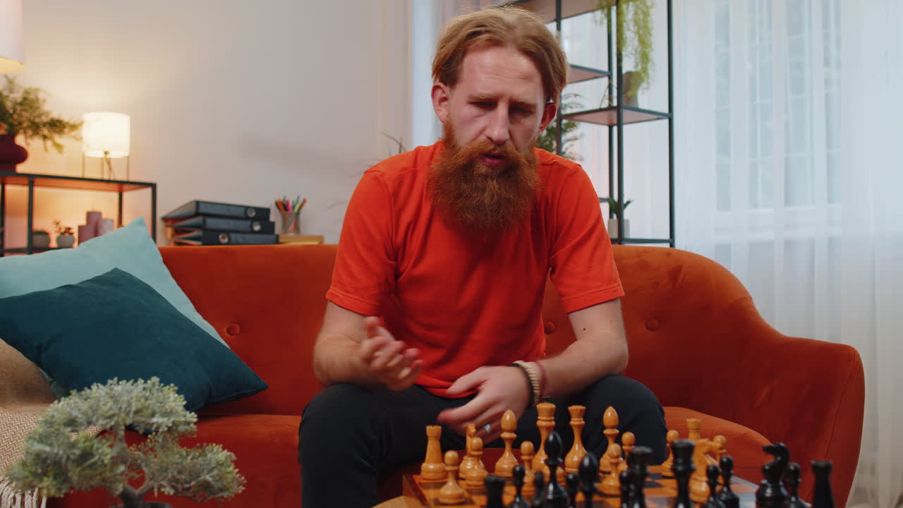 joven pelirrojo barbudo enfocado jugando al ajedrez juego de mesa de ocio solo, actividad doméstica en casa