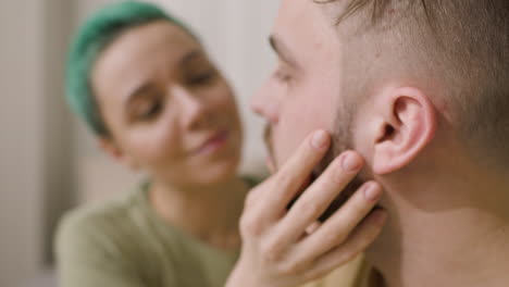 close up of a loving woman gently touching her boyfriend's face while sitting together on the bed