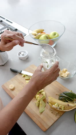 vertical video of senior biracial man preparing smoothie in kitchen at home