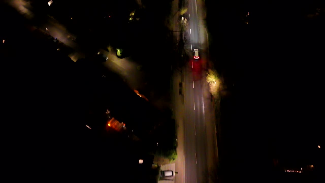 Apartment town houses at night. Aerial view of a quiet suburban street with two-story houses. Driving white car on illuminated street. Aerial top down tracking shot.
