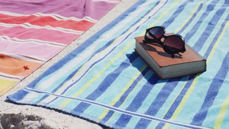 video of sunglasses, book, towels and beach equipment lying on beach