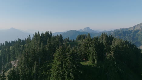 Aerial-footage-flying-over-the-peak-of-a-mountain-revealing-a-meadow-amongst-the-trees-in-the-morning-haze-in-the-Cascade-Mountains-in-Washington