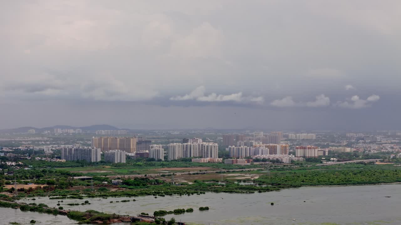 Moving drone view of clustered tall residential buildings with a body of water in front.