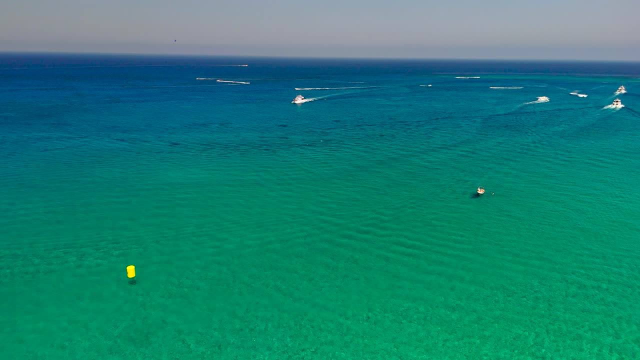 Bright sunlight shines on the clear turquoise waters as boats glide across the surface. People enjoy a beautiful day at the beach, embracing the warm weather