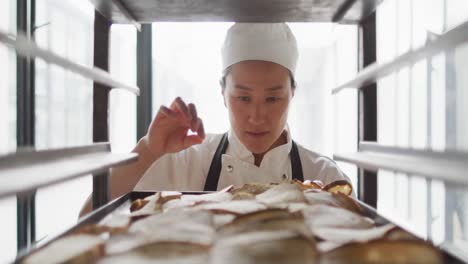 animation of happy asian female baker checking freshly prepared rolls