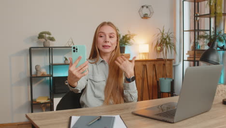 caucasian mature woman freelancer using smartphone having video call smiling while sitting at table