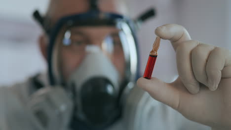 A-scientist-doctor-at-a-pharmaceutical-company-developing-a-drug-in-a-laboratory-in-a-glass-respirator-screen-holds-a-new-medicine-a-red-amulet-with-a-vaccine-against-the-virus-and-looks-at-it.-High-quality-4k-footage