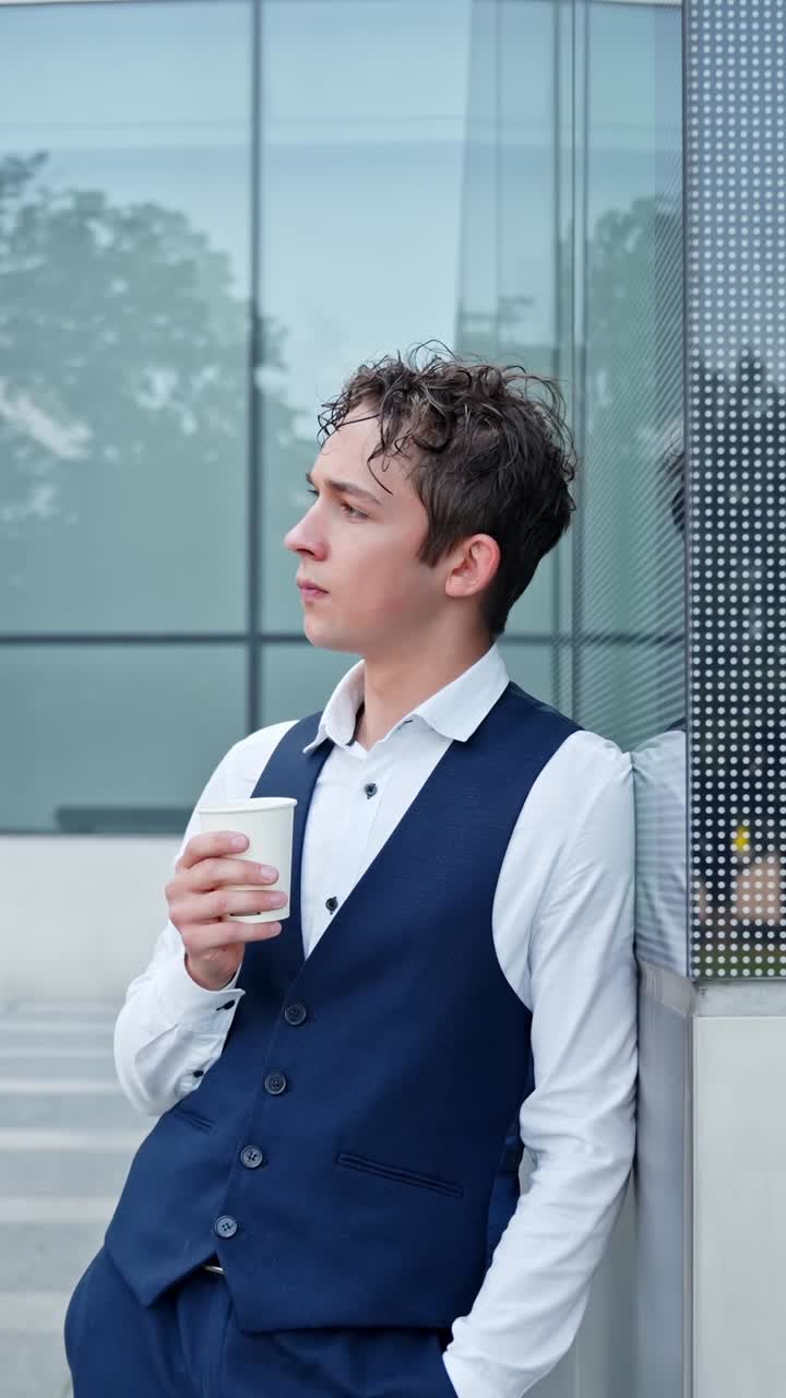 Camera pulls back from young businessman holding coffee outside modern office