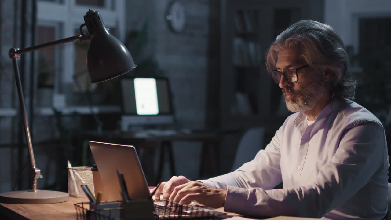 Man working on laptop at night in a dimly lit office