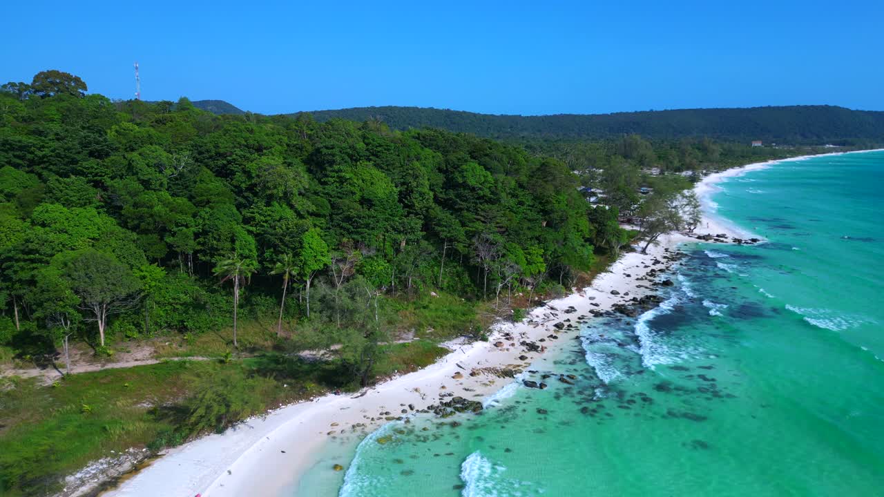 Black Stones in turquoise water gently washing the white sand beach of Koh Rong island, cambodia, on a sunny day with clear blue sky. Gorgeous aerial view flight static tripod hovering drone