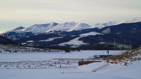 Gefrorener-Lake-Dillon-Frisco-Silverthorne-Breckenridge-Summit-County-Gefrorener-Neuschnee-Eisbahn-Früher-Sonnenaufgang-Winter-Colorado-Marina-Berggipfel-Landschaft-Langsam-Filmisch-Schwenk-Nach-Links