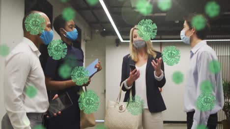 animation of covid-19 cells against diverse businesspeople wearing face masks discussing at office