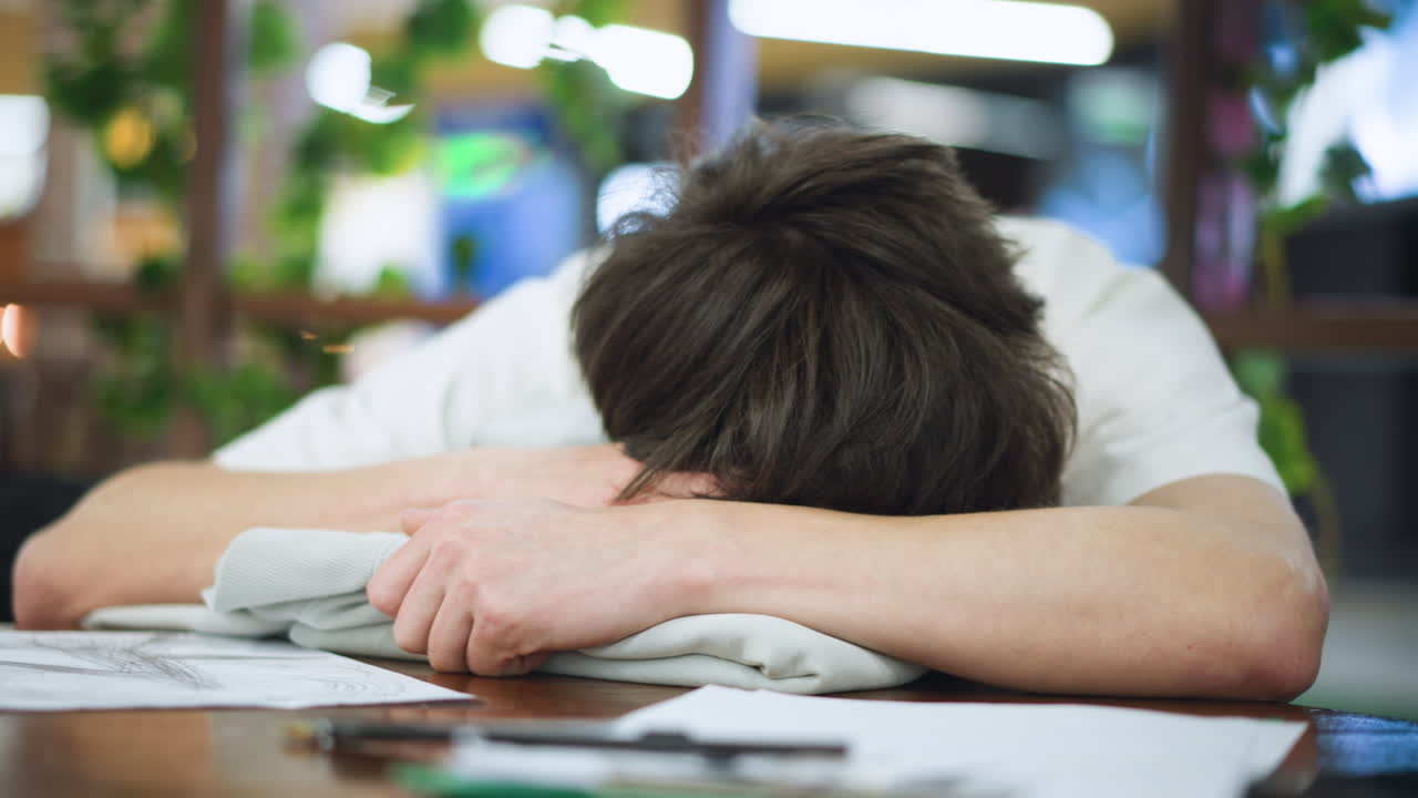 Camera pans close on teen in white polo resting head on table eyes closed for quick nap silent study break captured intimate mood with warm lighting subtle blur of calm atmosphere in indoor scene