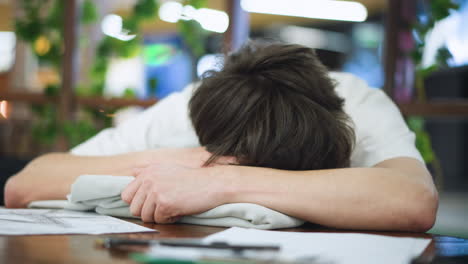 camera pans close on teen in white polo resting head on table eyes closed for quick nap silent study break captured intimate mood with warm lighting subtle blur of calm atmosphere in indoor scene