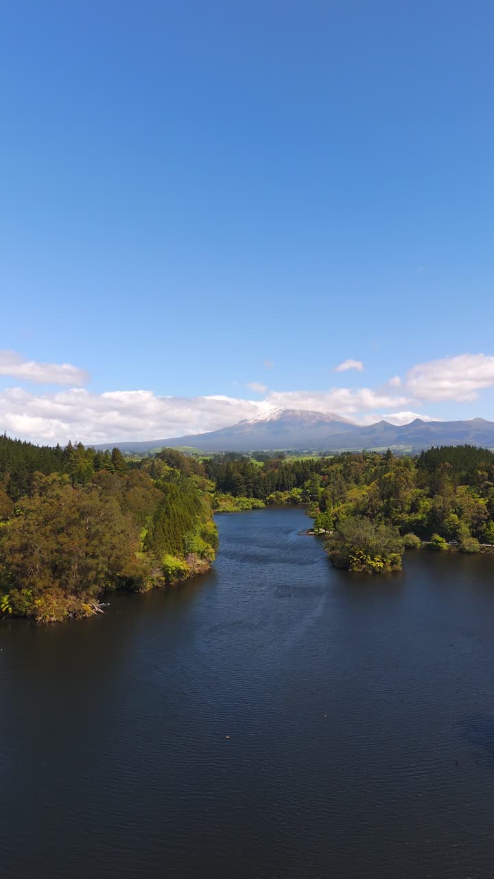 Lo stratovulcano Monte Taranaki si erge oltre il Lago Mangamahoe, circondato da un paesaggio forestale in Nuova Zelanda, ripresa aerea verticale con carrellata.