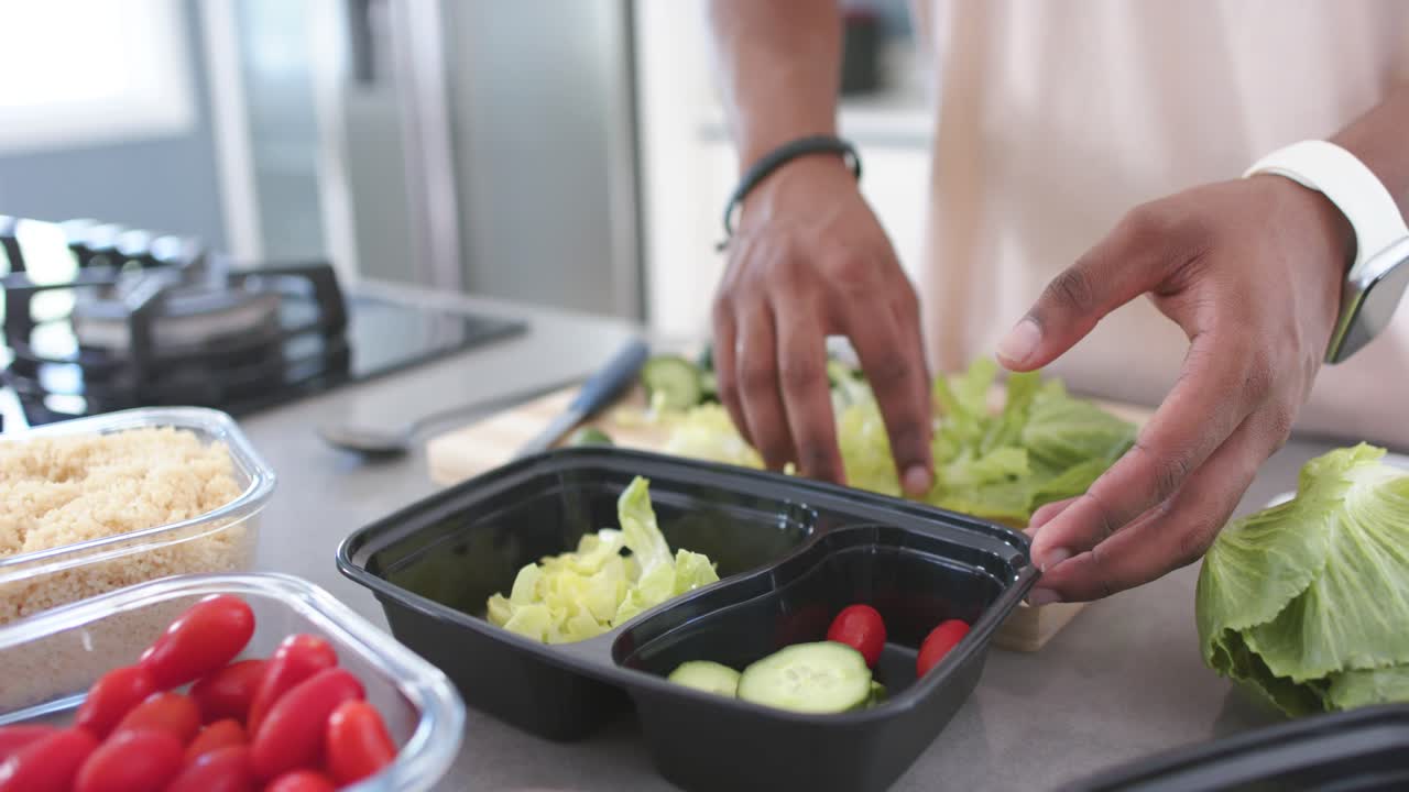African-American man packing shredded lettuce into black box from wooden board smoothing for lunch