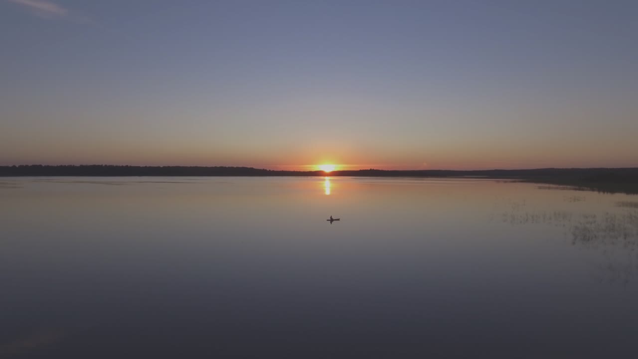 vuelo aéreo sobre un pescador en un bote en un lago en una tranquila tarde de verano al atardecer