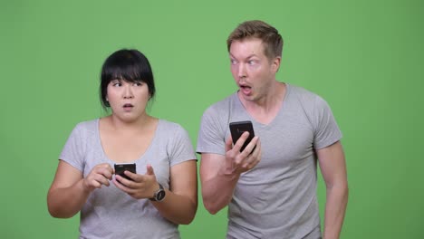 young multi-ethnic couple using phone and looking shocked together