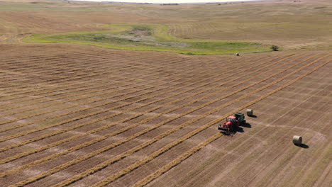 Aerial-View-Of-A-Tractor-Baling-Hay-At-The-Field-In-Saskatchewan,-Canada---orbiting-drone-shot