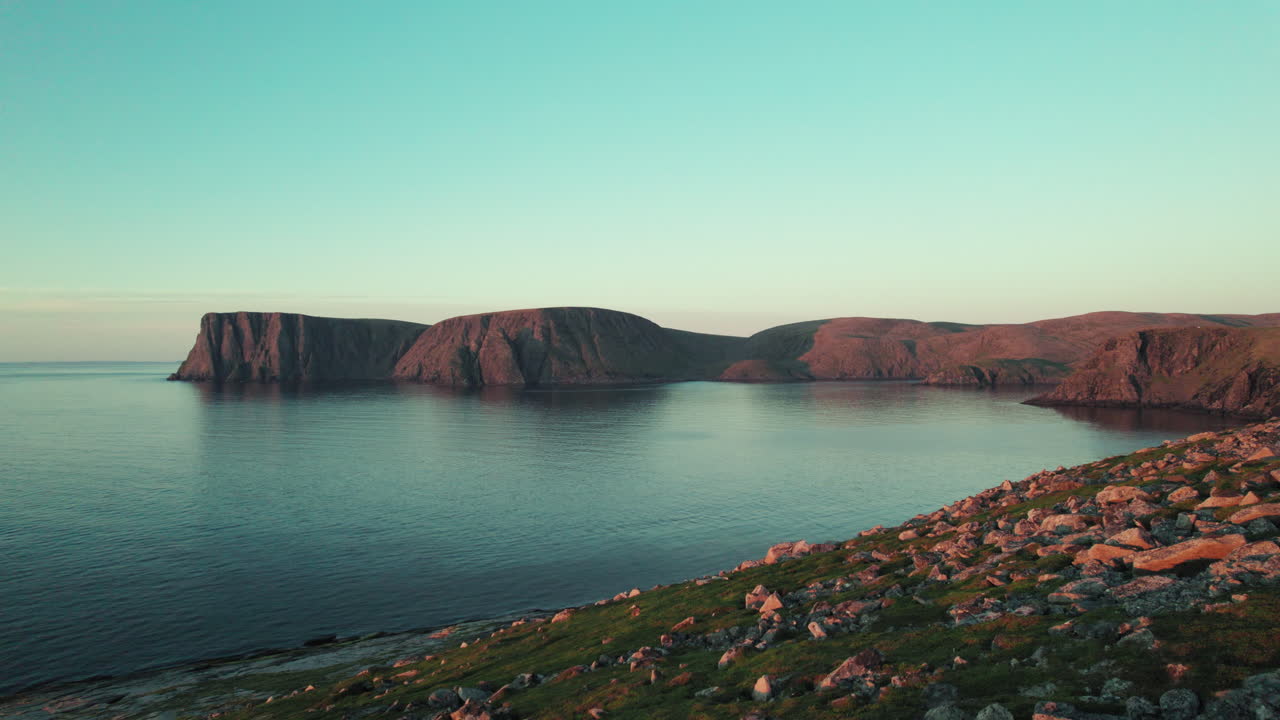 Ilmakuva rantaviivasta kauniissa auringonlaskun tunnelmassa Pohjois-Norjassa, norjalainen kallio-/jyrkännemaisema, drone matalalla maanpinnan yläpuolella, Nordkapp, Skandinavia