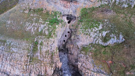 aerial: close circle of man made cave in the side of cliff, culver hole, port eynon, gower, 4k drone