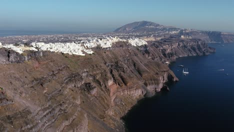 Panoramic-Aerial-of-Imerovigli-Village-Coast-Cliff-and-Sailboat,-Santorini