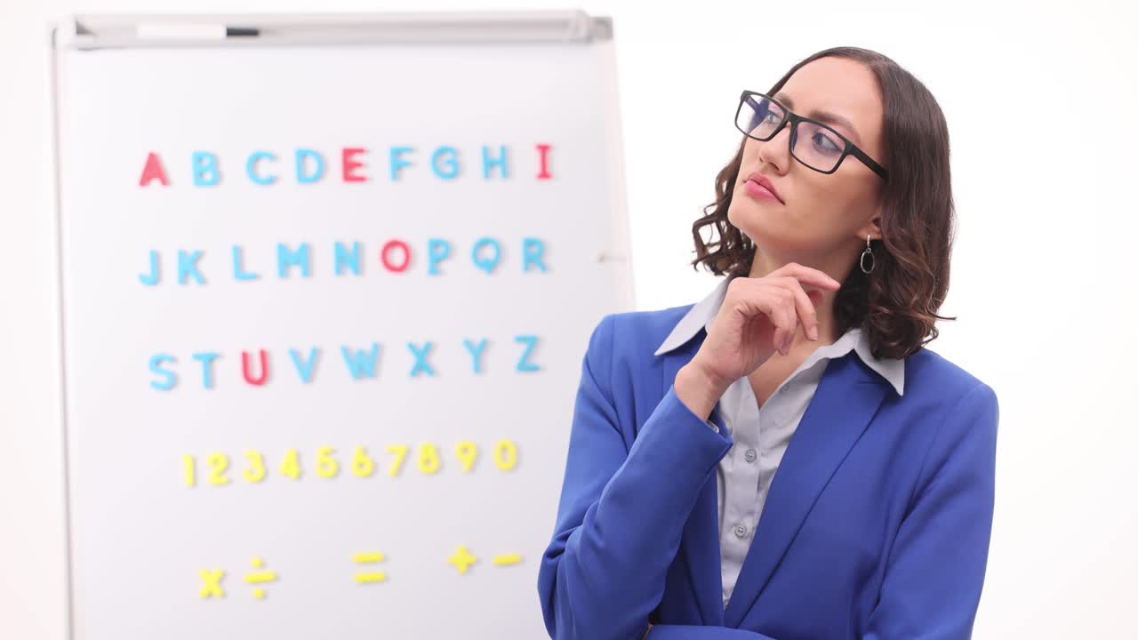 Teacher standing next to whiteboard with alphabet and numbers
