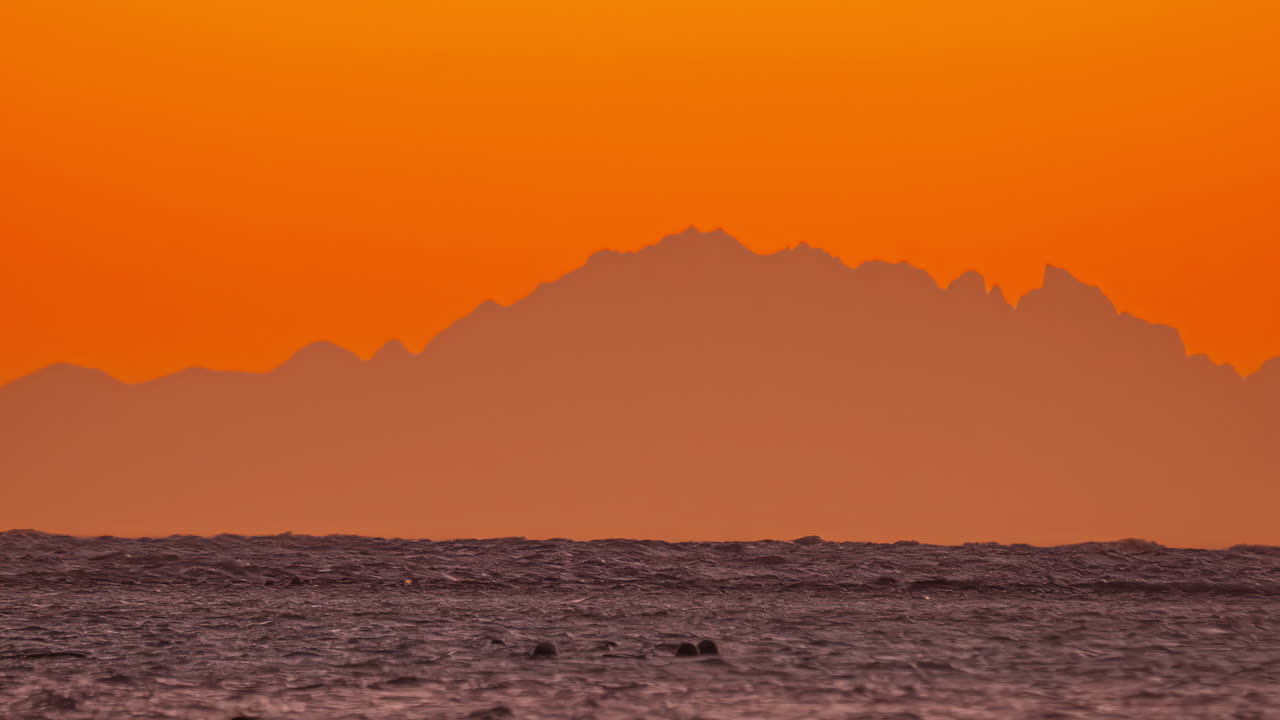 cielos naranjas vívidos sobre una cordillera escarpada con vista al océano timelapse