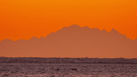 vivid orange skies over a rugged mountain range with ocean view timelapse