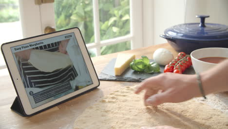 person following pizza recipe using app on digital tablet