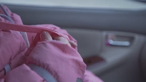 Mädchen-Spielt-Mit-Rosa-Winterjackengürtel,-Der-Im-Auto-Sitzt