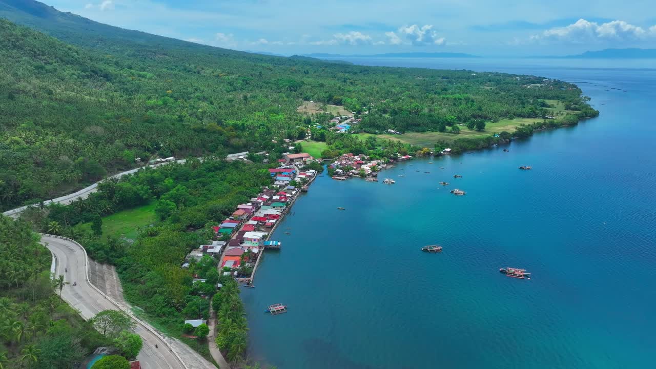 Houses and homes on coast of Carigara Bay on Biliran Island, Philippines. Boat and ship parking in bay. Green mountain landscape. Aerial wide shot.
