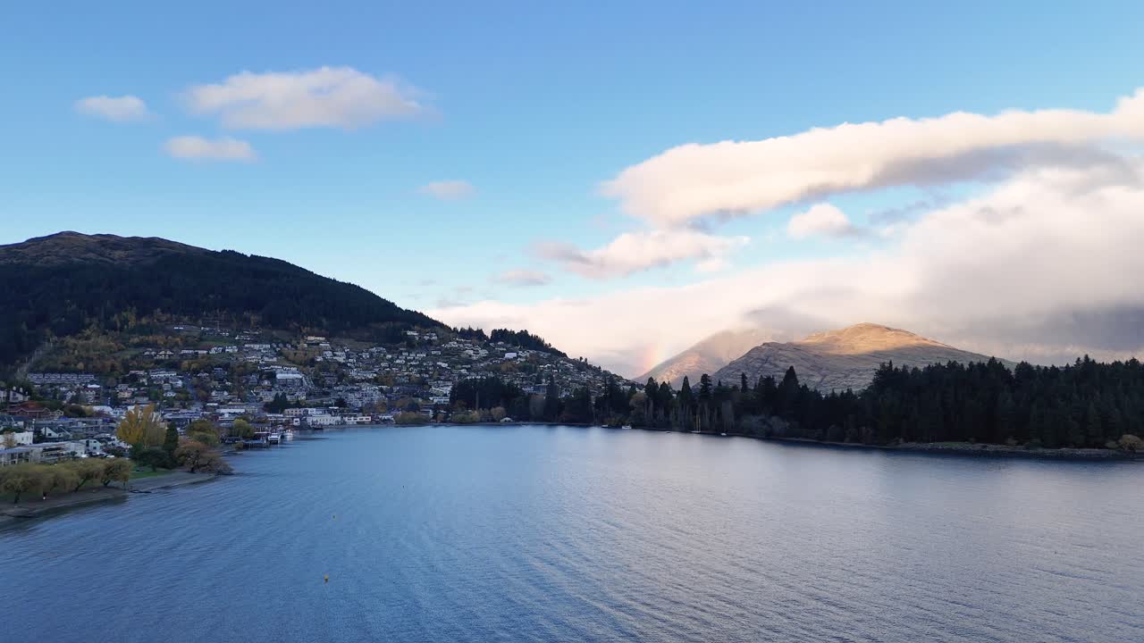 Aerial footage captures Queenstown's serene lake, surrounded by mountains under a partly cloudy sky, showcasing natural beauty and tranquility