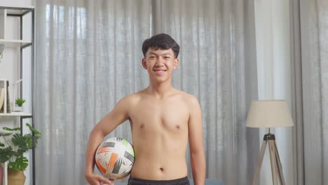 asian teenager boy with football smiling to camera after the shirtless workout at home