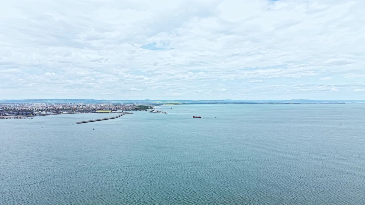 Vista del mare e della terraferma con navi in lontananza in una giornata nuvolosa, vicino alla costa, con la linea costiera e una città visibili.