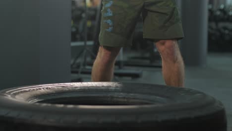 fit muscular man doing crossfit exercises of a sledgehammer striking a tractor tire in a gym