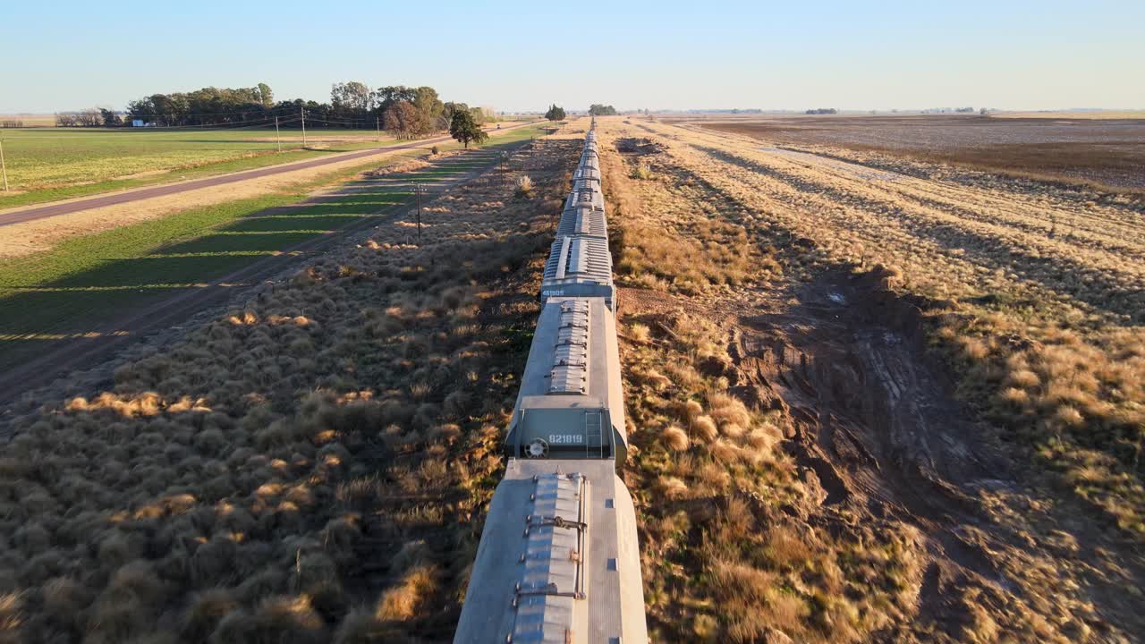 Aerial tracking follows along grain train moving through farmland in La Pampa, Argentina, during golden sunrise