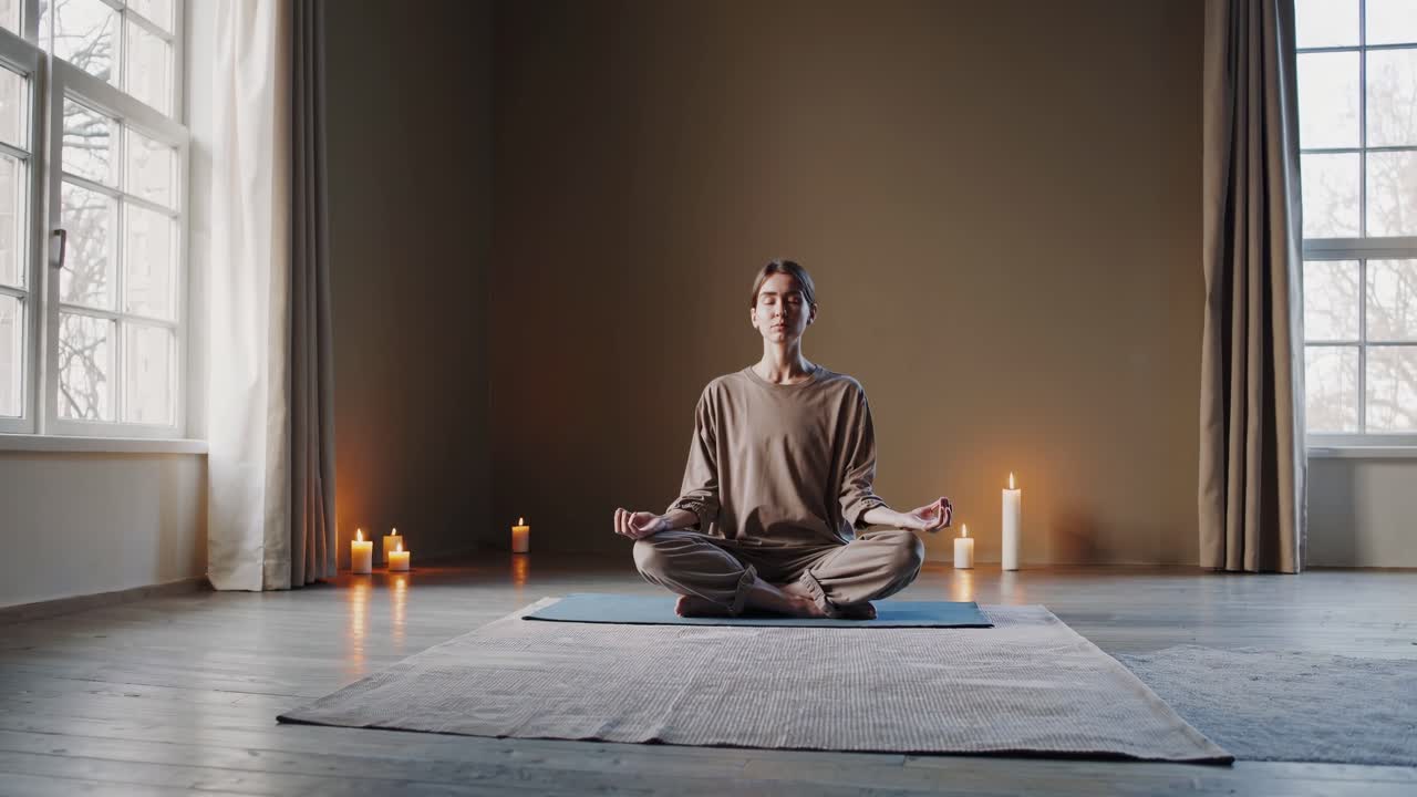 A serene yoga session video captures a woman meditating in a spacious room with candles, shot