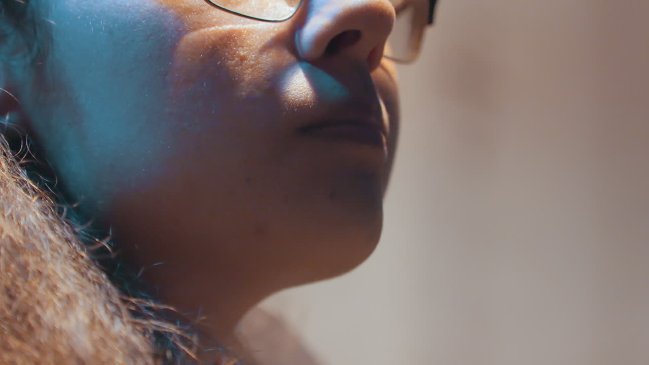 Closeup mouth and profile with glasses, warm interior light highlights subtle smile and breath, gentle chewing and exhale between bites, intimate cinematic texture and focused expression