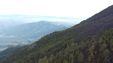 From-the-top-of-the-volcano-in-Guatemala,-flying-over-the-trees-and-city