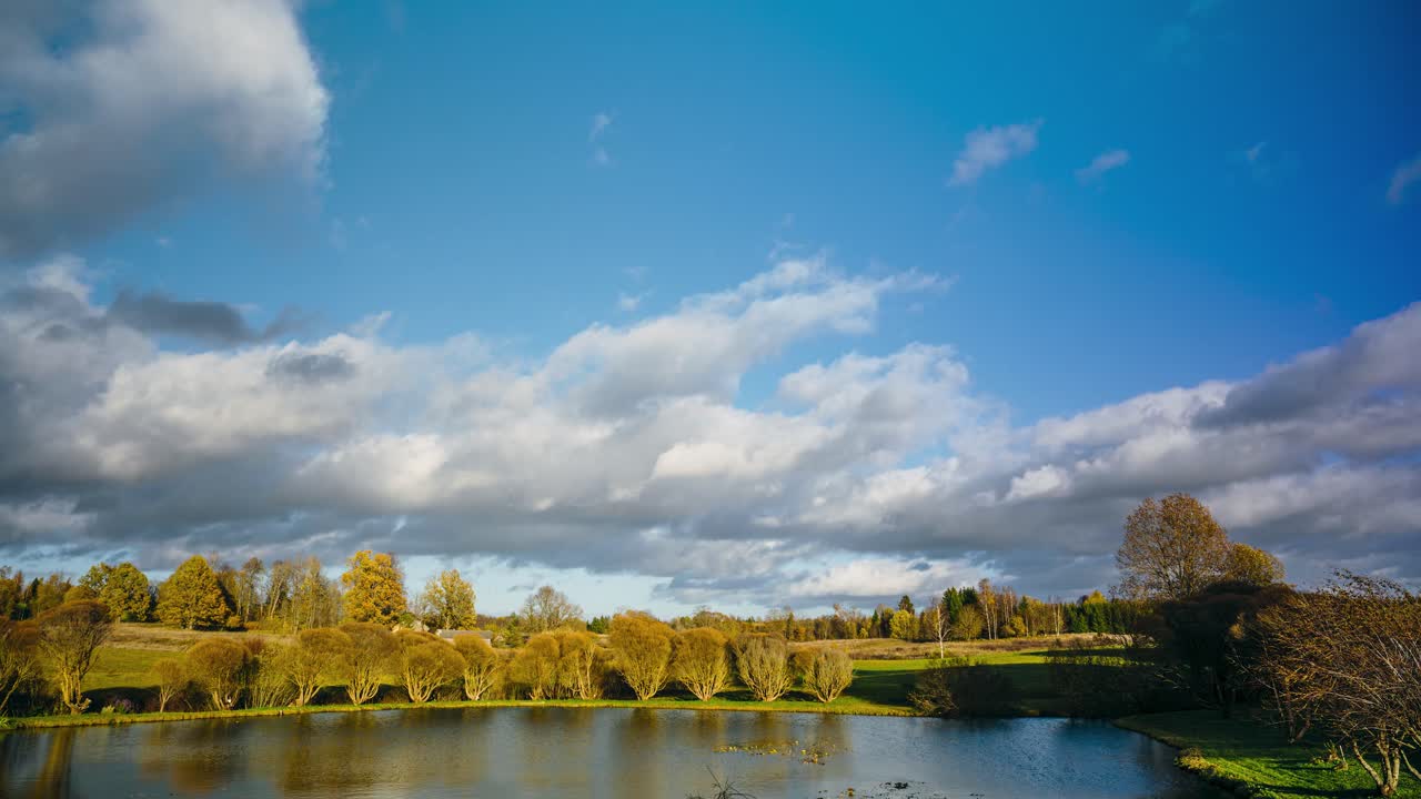 Fast pace cloudscape timelapse in autumn. Verdant countryside scenery with pond and forest in the background.