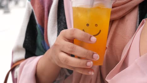 woman holding a cup of orange juice with a smiley face