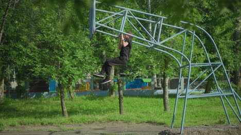 un niño vestido con un traje negro está realizando pull-ups en equipos al aire libre, rodeado de un entorno verde exuberante con árboles y una valla en el fondo