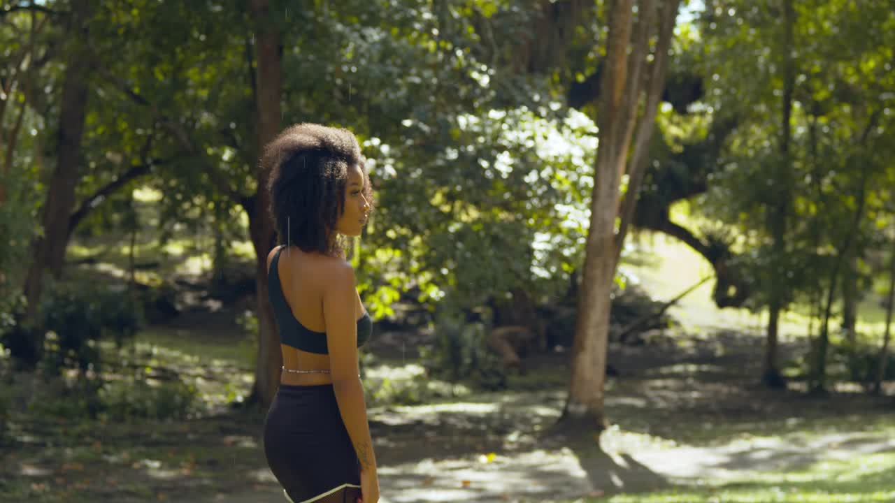 un modelo de cabello natural camina en un parque con gotas de lluvia cayendo de un árbol de algodón de seda