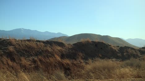 conduciendo por el desierto vacío con plantas secas pasando por el lado de la carretera con colinas y montañas en la distancia, más cerca
