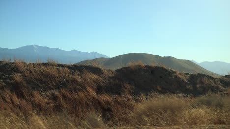 driving through the empty desert with dry plants passing by on the side of the road with hills and mountains in the distance, closer